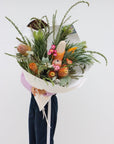 An amazing sized seasonal native bouquet. The pictured bouquet includes a variety of banksias (6 total), large silver leucadendrons, knife wattle, gum/eucalyptus foliage, a protea and strawflowers. The bouquet is gift wrapped in white paper and is tied with a light pink ribbon.