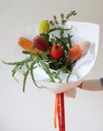 Bouquet of five assorted Banksia flowers wrapped in white paper with red and orange ribbon.