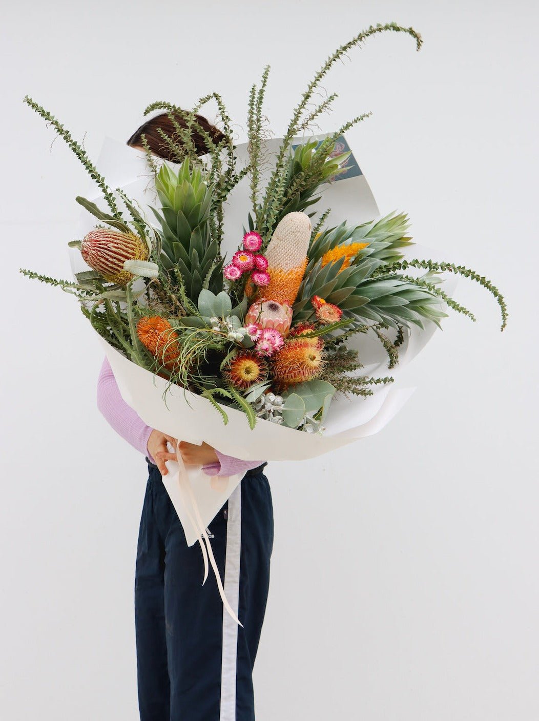 An amazing sized seasonal native bouquet. The pictured bouquet includes a variety of banksias (6 total), large silver leucadendrons, knife wattle, gum/eucalyptus foliage, a protea and strawflowers. The bouquet is gift wrapped in white paper and is tied with a light pink ribbon.  