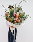 An amazing sized seasonal native bouquet. The pictured bouquet includes a variety of banksias (6 total), large silver leucadendrons, knife wattle, gum/eucalyptus foliage, a protea and strawflowers. The bouquet is gift wrapped in white paper and is tied with a light pink ribbon.  