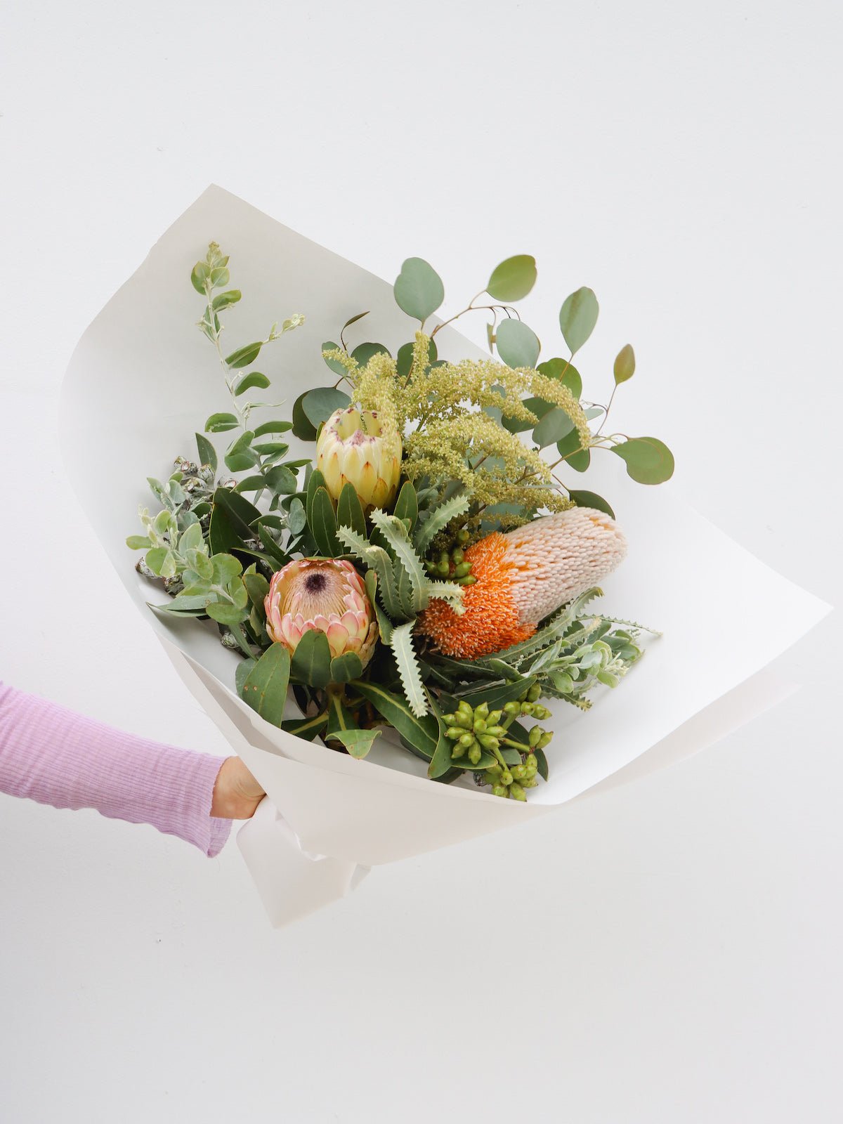 A small sized seasonal native arrangement featuring 2 banksias, a protea, gum and wattle foliage. This arrangement is wrapped in white paper. 