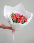 A bouquet of pink double tulips gift wrapped in white paper and tied with a pink ribbon. 