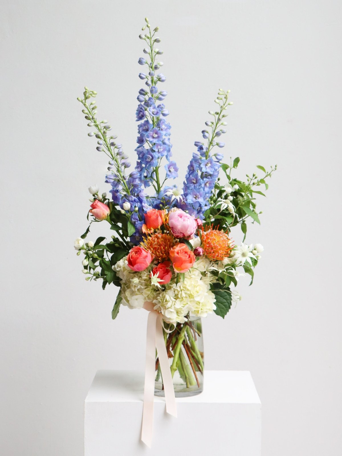 A large seasonal arrangment in a glass vase. The arrangement in this image features Pincushions, Roses, Hydrangea, Flannel Flowers, Delphinium, Peonies and Mock Orange. 